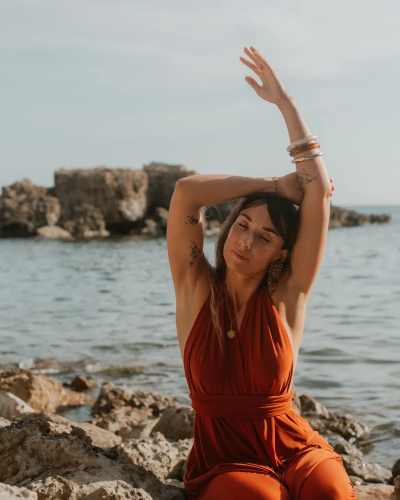 Marine in a red dress by the sea, arms raised
