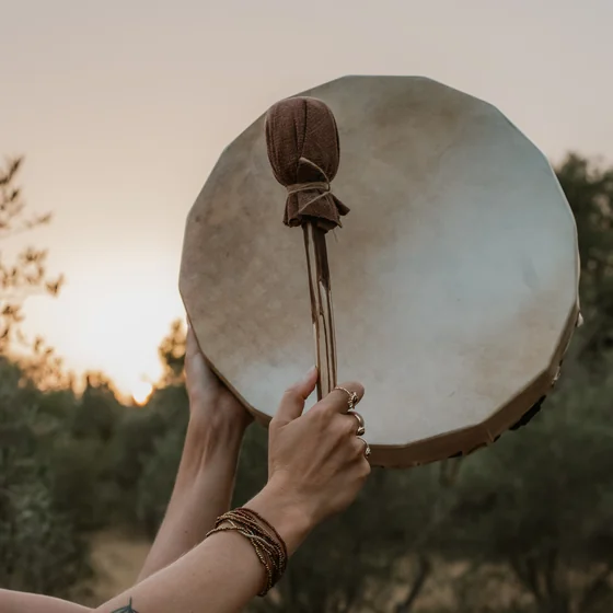 Un tambour chamanique tenu vers le ciel au crépuscule